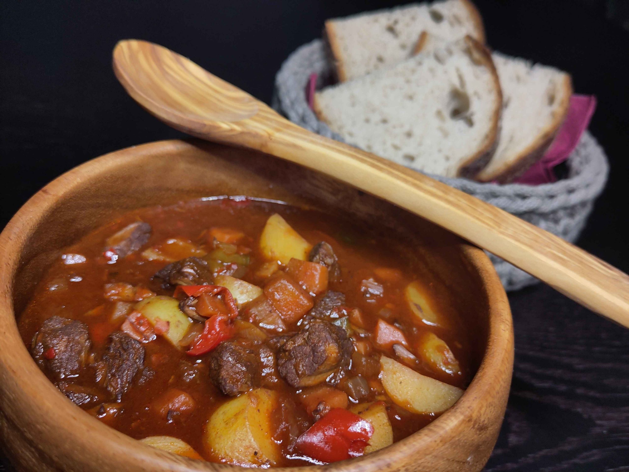 Gulaschsuppe in einer Holzschüssel mit Holzlöffel und dazu dicke Brotscheiben
